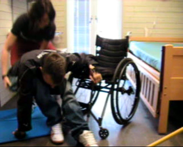 En hjälpperson håller användaren under sittknölarna och lyfter ner honom till golvet