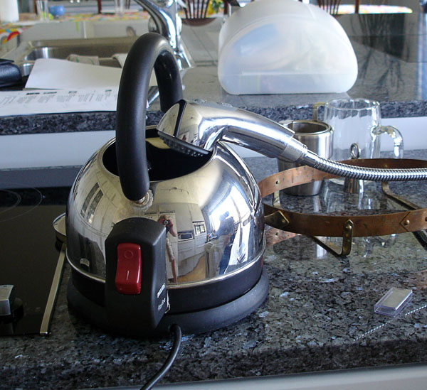 A kettle standing on the sink is filled with the sprayer pulled out.