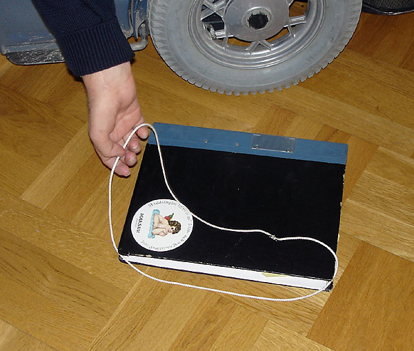 The user holds the string tied to a loop and slips it under a binder, which is lying on the floor.