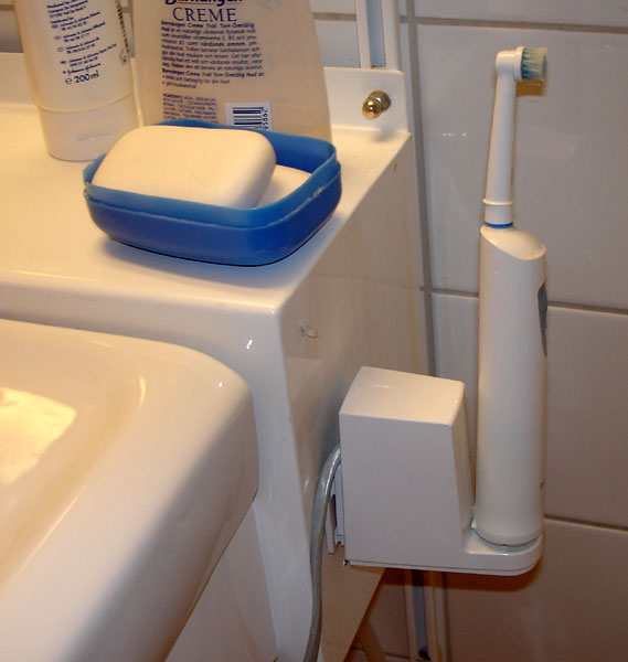 Electric toothbrush in holder attached to the side of the wash basin