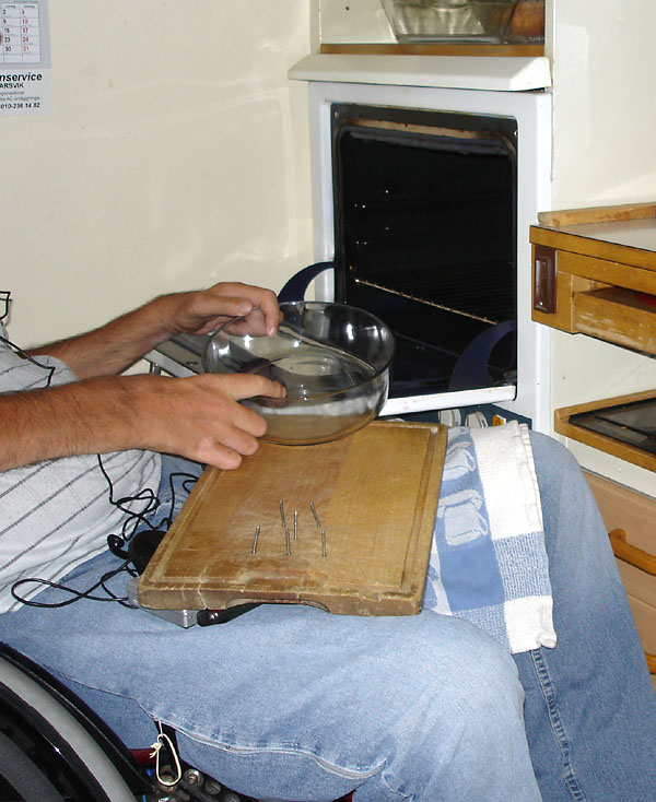 The user pushes an oven dish from a cutting board on his lap onto the open oven door