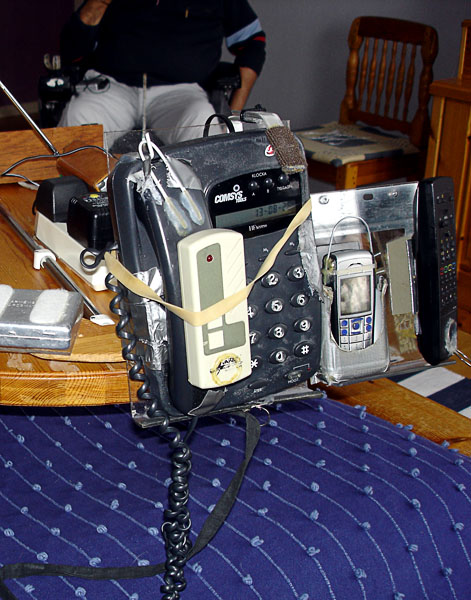 Speaker phone and mobile phone on holder, TV remote sitting attached to the telephone with a rubber band