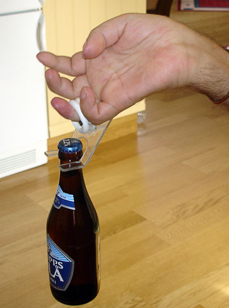 Användaren håller i en flaska med ringfingret i hjälpmedlets ring (närbild)