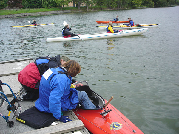 User moving into the kayak; a person holds the kayak