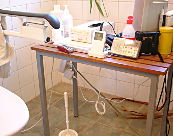 Table by toilet chair with radio, music player, and other things