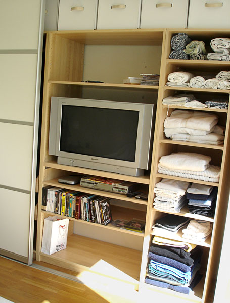 Wardrobe with open doors. Inside there are shelves with TV and music player, as well as towels, etc.