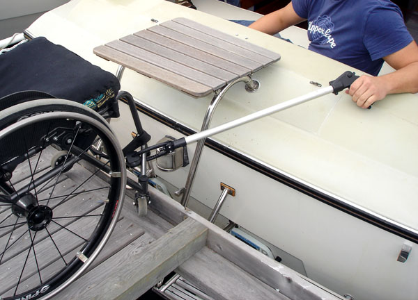 User sitting on boat and pulling wheelchair toward himself with reach extender