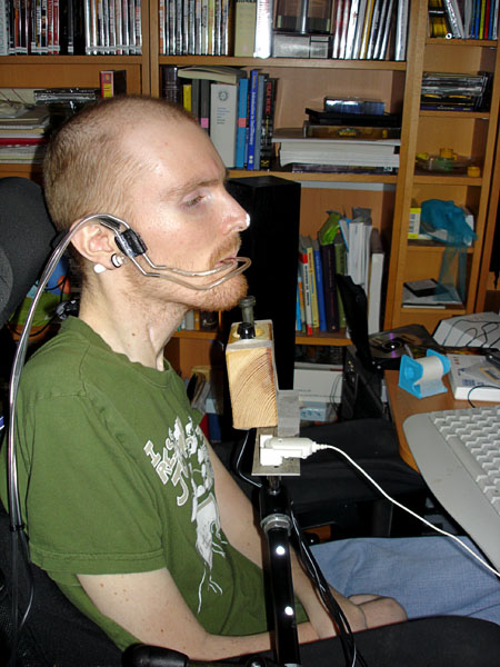 The user sits in front of the computer. He has a joystick mounted in a custom-made wooden block against his chin.