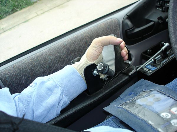 User's arm and hand on the car's forearm support plate with accelerator and brake controls