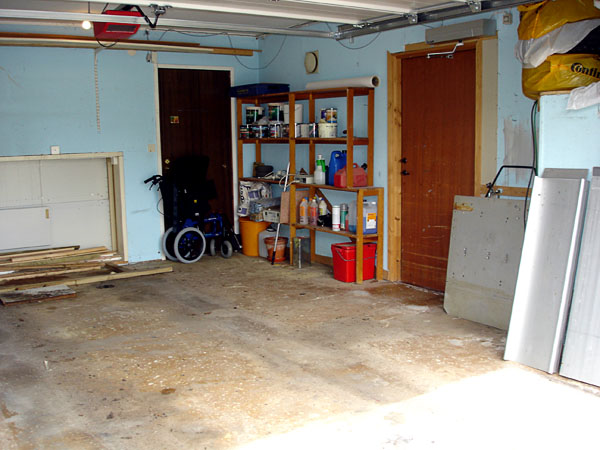Garage inifrån utan bil med uttag i väggen på främre kortsidan och sidodörr.