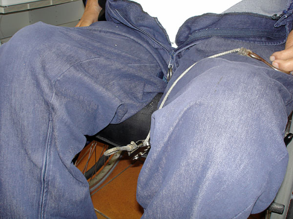 The user takes the steel hook and cord out from under the wheelchair and places it on his lap