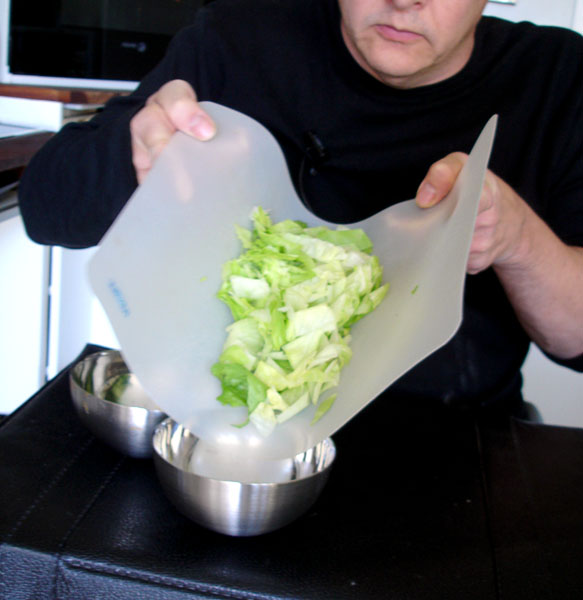 User pours lettuce into bowl using the folded cutting board