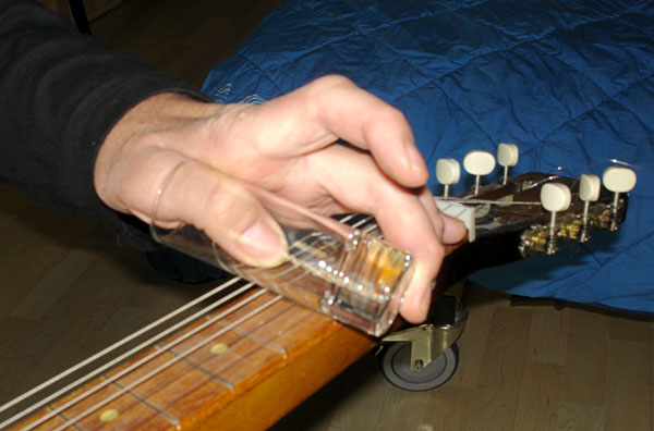 The user slides the slide on the guitar strings (close-up)