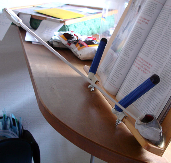 'Page turner - mouth stick' sitting in a holder (plastic tube) at a book stand