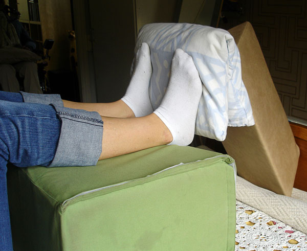 User lying on back with lower legs on square pillow, long narrow wedge pillow angled towards feet