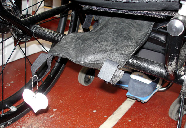 Catheter bag under wheelchair seat with open attachment strap (from the back)