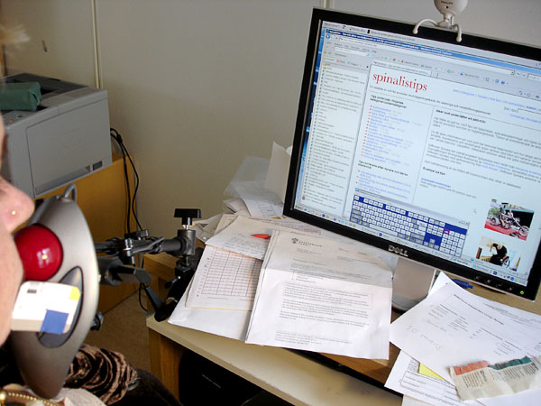 Bordsfäste med trackbålmus står mot Helenas haka. På dataskärmen framför henne syns ett on-line tangentbord.