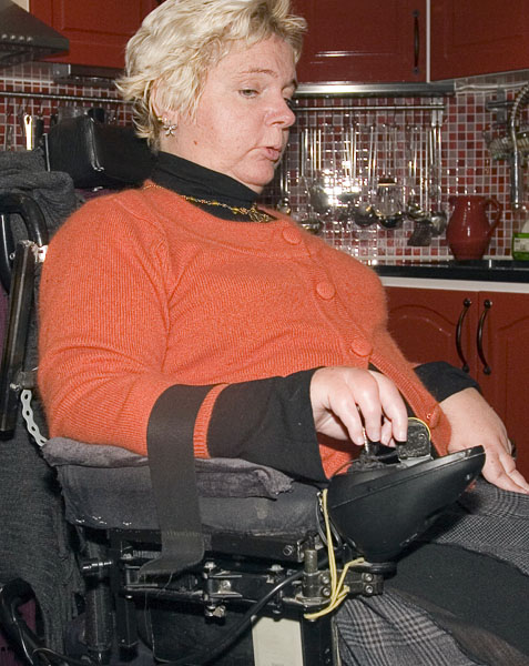 Helena drives wheelchair; her forearm is attached to the armrest with a strap