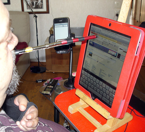 In front of the user is his iPad on a stand, he controls the iPad with a mouth stick.