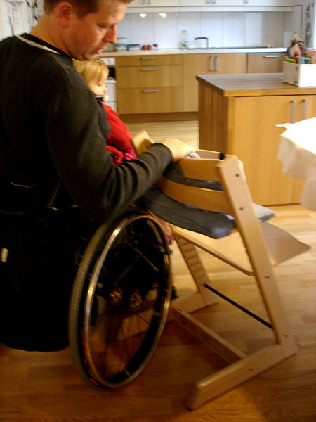 The user is positioned diagonally behind the highchair to move his daughter over