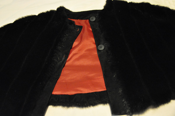 Faux fur cape Attached edge with buttons is visible.