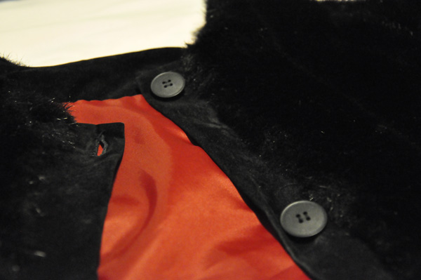 Påsatta kanter med knappar och onapphål  på cape i fuskpäls (närbild). 