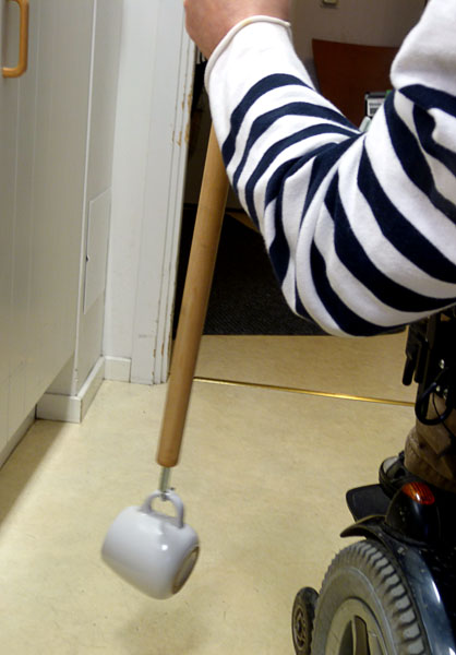 Användaren plockar upp en kopp från golvet med hjälp av en anpassad pinne
