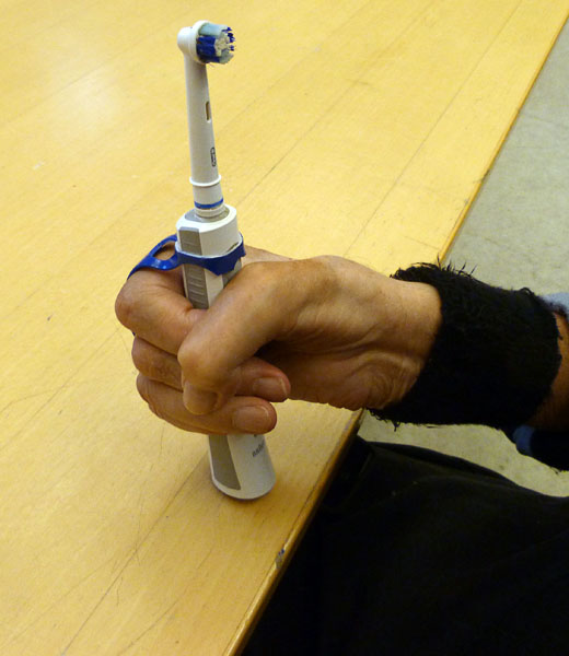Användaren håller i sin tandborste med hjälp av hålband i plast som är fastsatt på el-tandborsten som ett handtag. 