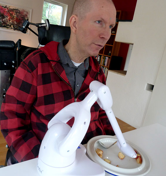 User sitting at dining table with Bestic (movable arm with spoon) and special plate in front of him
