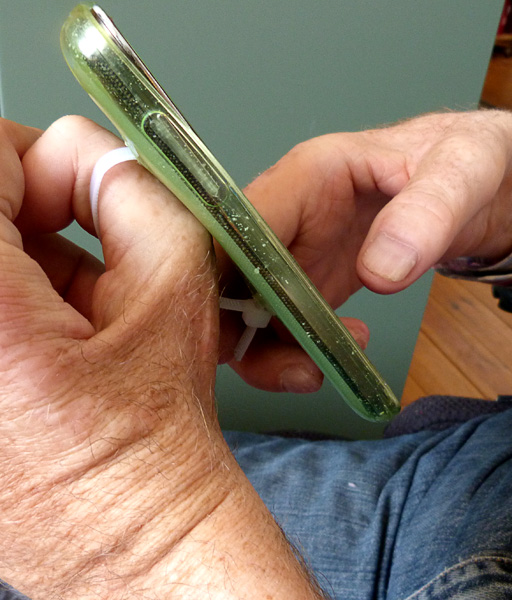The user holds his phone with his thumb in the loop of cable tie. 