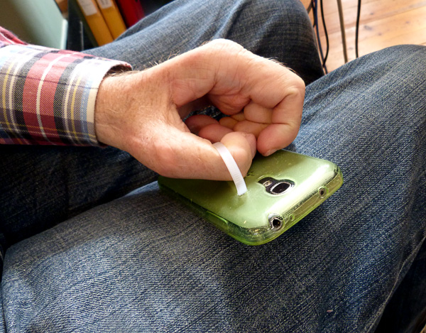 Användaren tar upp sin telefon genom att trä in tummen i öglan av buntband