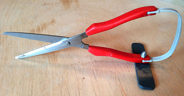 A small plastic piece is attached to a handle that protrudes at 90 degrees and allows the scissors to stand on a handle.