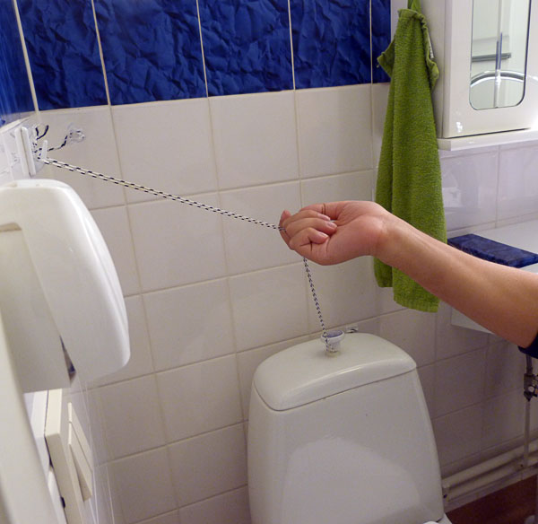 The user pulls a string attached to the toilet flush button and to a hook on the wall.